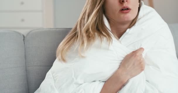 Close-up van ongezonde blanke slecht uitziende jonge vrouw zitten op de bank verpakt in deken en meten temperatuur. Meisje met griep of coronavirus heeft koorts. Vrouw in zelfisolatie. — Stockvideo