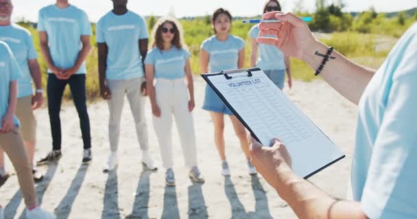 Gros plan d'un presse-papiers avec la liste des bénévoles. Le leader divise les responsabilités et vérifie la présence des membres, des participants. Concept de conservation de la nature et de l'environnement Sauver l'écologie. — Video