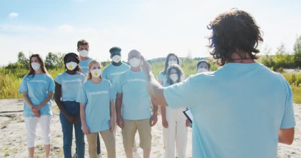 Volunteer mentor giving instructions on garbage, litter, rubbish, trash, waste collection. Enthusiastic nature protectors in masks listening to the leader and raising hands. Ecology, emission concept. — Stock Video
