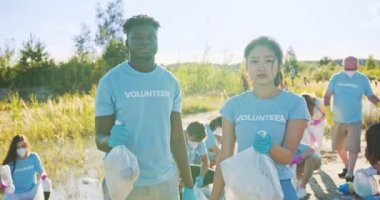 Kumsalı çöplerden temizleyen gönüllü bir örgüt üyesi. Çöp torbaları tutan ve kameraya bakan çok ırklı çevreci aktivistler. Biyosfer, ekoloji koruma kavramı.