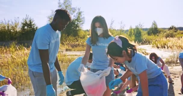 Jóvenes voluntarios altruistas recogiendo basura, basura y metiéndola en bolsas de basura. Activistas multiétnicos masculinos y femeninos limpiando la naturaleza de la contaminación. Contaminación, concepto de supervivencia ecológica. — Vídeos de Stock