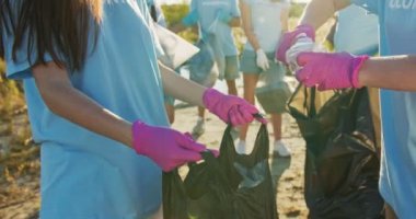 Güzel beyaz kadın gönüllüler çöp torbasında çöp topluyor. Eldivenli genç kadın çevreciler plastik şişe bastırıyor, kameraya bakıyor ve gülümsüyor. Geri dönüşüm, kirlilik kavramı.