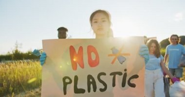Plastik kullanımını protesto eden genç Asyalı gönüllü bir bayan. Bir grup çok ırklı çevreci, Plastik Yok posteriyle yürüyor. Geri dönüşüm, doğa koruma, kirlilik kavramı.