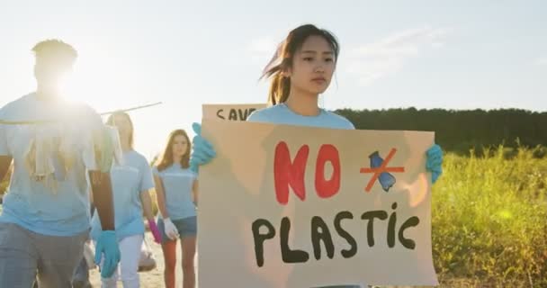 Un'organizzazione volontaria che protesta contro l'utilizzo della plastica. Un giovane e paziente volontario asiatico che cammina con un poster No Plastic e guarda la macchina fotografica. Inquinamento, concetto di contaminazione. — Video Stock