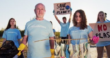 Plastik kullanımını ve ekoloji kirliliğini posterlerle protesto eden farklı yaşlarda bir gönüllü. Büyük ve genç kız gönüllü ellerinde çöp ve tıbbi maske tutuyorlar. Doğa koruma.