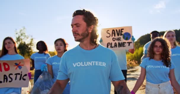 Grupo de voluntarios multiétnicos con carteles protestando contra la contaminación y la utilización del plástico. Atractivo adulto caucásico activista masculino sosteniendo utiliza máscaras médicas y mirando a la cámara. Ecología. — Vídeos de Stock