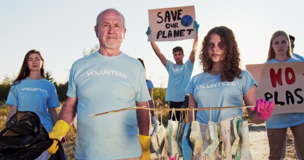 Különböző korú önkéntes tiltakozik a plakátokkal történő műanyagfelhasználás és környezetszennyezés ellen. Végzős és fiatal önkéntes lány, aki szemetet tart és orvosi maszkot használ. Természetvédelem. — Stock videók