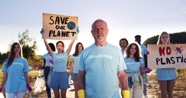 Un grupo de voluntarios con afiches Save Our Planet y No Plastic. Un hombre mayor eco activista sosteniendo una bolsa de basura y mirando a la cámara. Conservación ambiental, concepto de contaminación. — Vídeo de stock