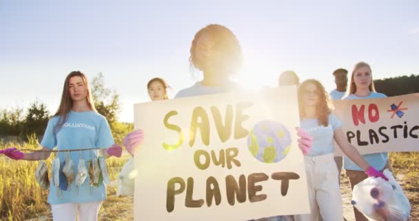 Krásná africká dobrovolnice drží plakát Save Our Planet a dívá se do kamery. Skupina multietnických aktivistů protestujících proti znečištění přírody. Ekologie, koncepce biosférické ochrany. — Stock video