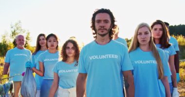 Bir grup melez gönüllü çevreyi koruyor. Farklı yaşlardan çevre aktivistleri elinde çöp kutusuyla kameraya bakıyor. Gönüllülük, doğa koruma, ekolojik sorun, kirlilik.