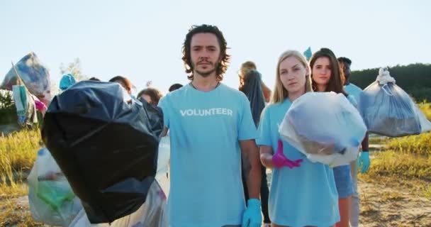 Un grupo de activistas de la naturaleza después del trabajo de recolección de basura. Miembros de una organización voluntaria mirando a la cámara y levantando basura, bolsas de basura. Naturaleza, concepto de protección ecológica. — Vídeo de stock