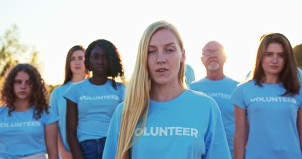 Giovane donna attraente con un gruppo di eco attivisti sullo sfondo. Una volontaria abbastanza caucasica che guarda la telecamera e dice: Sono una volontaria. Volontariato, conservazione dell'ambiente. — Video Stock