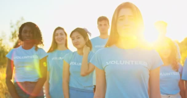 Retrato de mulher jovem atraente com grupo de eco ativistas em segundo plano. Bonita voluntária caucasiana olhando para a câmera e dizendo: Eu sou voluntária. Voluntariado, conservação do ambiente . — Vídeo de Stock