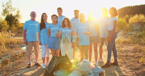 A group of multiethnic nature volunteers conserving environment. Ecology activists after collecting garbage standing with trash bags and looking at camera. Environmental conservation concept. — Stock Video