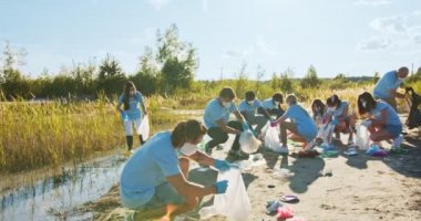 Arka planda bir grup çevreci aktivistle birlikte maskeli bir adam çöpleri çöp poşetine atıyor. Erkek bir gönüllü plastik şişe, mukavva ve atık topluyor. Ekoloji koruma kavramı.
