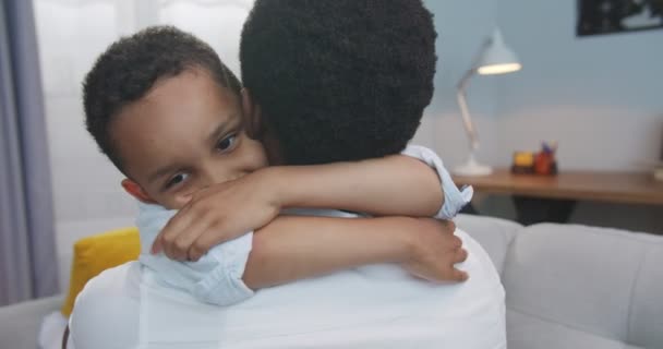 Close up portrait of cute little African American child hugging his father at home. Rear of man hugs happy small boy in living room indoors. Lovely family relations. Happiness concept — Stock Video