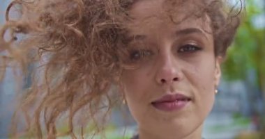 Güzel, genç bir bayanın kıvırcık saçlarında esen serin rüzgar. Soluk soluğa kalmış açık kahverengi saçlı, kameraya bakan, gülümseyen beyaz iş kadını. Refah yaşam tarzı konsepti.