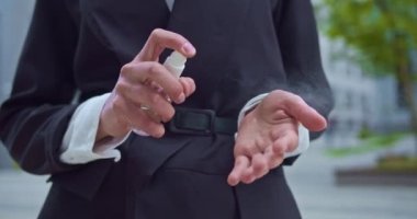 Resmi siyah takım elbiseli bir iş kadınının fotoğrafını çek. Bir ofis çalışanı ellerini antiseptik ve dezenfektanla dezenfekte ediyor. Sağlık, salgın, salgın, koronavirüs. Modern binaların arka planı.