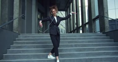 Gülümseyen genç bayan işçi iş bölgesinde akıllı telefondan müzik dinliyor. Güzel iş kadını kulaklıklarla ve açık havada dans ederek müziği seviyor. İş, teknoloji..