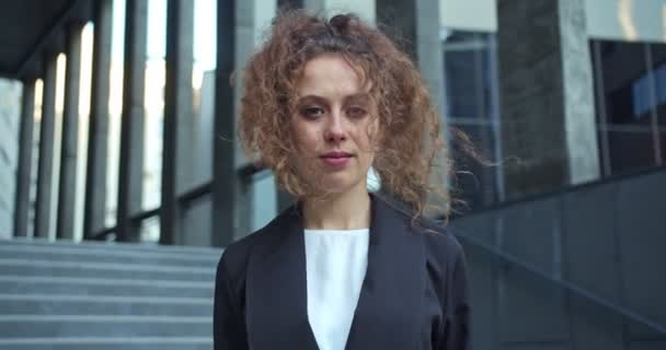Ofis binasının dışında duran güzel bir iş kadınının portresi. Çekici kıvırcık saçlı kadın finans, kameraya bakan kanun adamı. Girişimcilik, iş kavramı. — Stok video