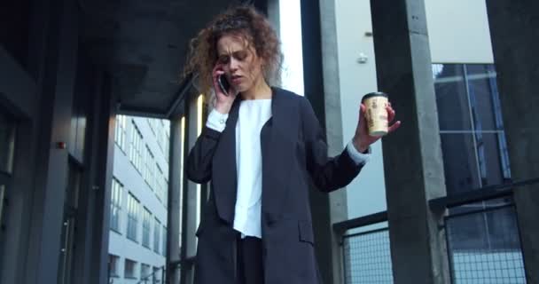 Charmig kvinnlig kontorsarbetare i en formell kostym som går ner för trappan med en kaffekopp. Snygg vit affärskvinna med solglasögon som pratar i telefon och skyndar sig. Arbetsdagar. — Stockvideo