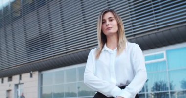Açık havada duran çekici beyaz iş kadınının portresi. Caddedeki ofis binasının önünde beyaz bluzlu neşeli genç bir bayan işçi. İş konsepti