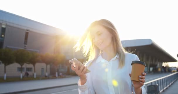 Primer plano de alegre hermosa joven trabajadora caminando en la ciudad con café y tocando en el teléfono inteligente. Caucásico mujer feliz escribiendo y buscando en Internet en el teléfono celular al aire libre. Concepto de retrato — Vídeos de Stock