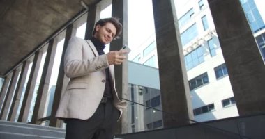 Alttaki manzara mutlu beyaz erkek profesyonel dışarıda dururken daktilo ediyor ve akıllı telefonları dinliyor. Caddede cep telefonuyla mesaj atan ve gülümseyen yakışıklı bir genç. İş konsepti