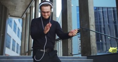 Kafkasyalı mutlu genç adam kulaklıkla müzik dinliyor ve merdivenlerde yürürken dans ediyor. Gözlüklü yakışıklı adam şarkılar dinliyor ve şehirde sokakta dolaşıyor. Eğlenceli konsept
