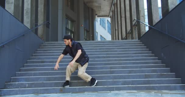 Glücklicher gutaussehender kaukasischer Typ führt modernen Hip-Hop-Tanz auf der Straße in der Stadt auf. Junger fröhlicher Mann tanzt gut gelaunt moderne Choreografien auf Treppen im Freien. Freestyle bewegt sich. Streetdance-Konzept — Stockvideo