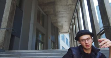 Kasabada dans eden şapkalı, kablosuz kulaklıklı yakışıklı beyaz çocuğun portresi. Gözlüklü genç bir sokak dansçısı. Modern koreografi açık havada merdivenlerde. Çağdaş dans. Konsepti kapat