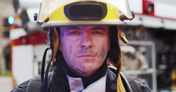 Gros plan portrait de beau pompier dans le casque et l'équipement de mouette debout à côté de la voiture avec des lumières clignotantes allumées et regardant dans la caméra. Concept de sauver des vies, profession héroïque, sécurité incendie — Video