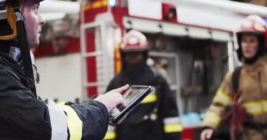 İtfaiyecilerin kasklı ve martı ekipmanlı portresi itfaiye aracının yanında duran kurtarma planını tartışıyor. İtfaiyeci yön gösteriyor. İtfaiye dumanı kurtarıcıları koruyor..