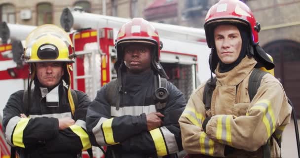 Portrait of three firefighters standing next to fire van in front of camera looking crossing hands after hard work. Concept of saving lives, heroic profession, fire safety — Stock Video