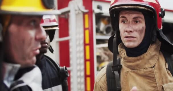 Primer plano retrato de bomberos en cascos y equipo de gaviota discutiendo plan de rescate de pie cerca de furgoneta de bomberos. Bombero mostrando dirección. Concepto de salvar vidas, profesión heroica, seguridad contra incendios — Vídeo de stock