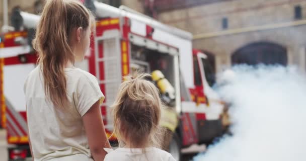 Portret van twee meisjes die brandweermannen zien vechten. Brandweerlieden in helmen en beschermende pakken in de rook redden mensen. Het concept van het redden van levens, heldhaftig beroep, brandveiligheid — Stockvideo