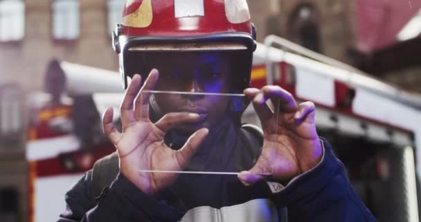 Portret van Afro-Amerikaanse brandweerman in helm en meeuw apparatuur die naast de auto staat en een doorzichtig scherm houdt terwijl hij iets op het digitale scherm bekijkt. Toekomstig technologieapparaat. — Stockvideo