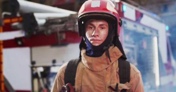 Portrait of firefighter approaches from fire van with flashing lights on and standing in front of camera looking after hard work. Smoke from fire covers rescuers. Concept of saving lives, fire safety — Stock Video