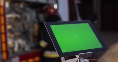 İtfaiyeciye yakın çekim, insansız hava aracından yayın yapan bir ekran kullanarak ateş ölçeğine bakar. İtfaiyenin arka planında yeşil ekran var. Hayat kurtarma kavramı, kahramanlık mesleği, yangın güvenliği.