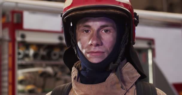Портрет белого красавца-пожарного в шлеме и чайке, стоящего рядом с машиной и смотрящего в камеру. Концепция спасения жизней, героической профессии, пожарной безопасности — стоковое видео