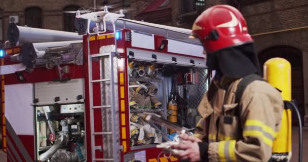 Portret strażaka używającego panelu kontrolnego drona do oceny zasięgu ognia. Ratownik stoi w pobliżu dużego czerwonego wozu strażackiego. Koncepcja ratowania życia, bohaterski zawód, bezpieczeństwo przeciwpożarowe — Wideo stockowe