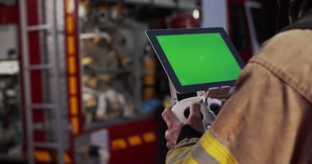 Portrét hasiče ovládajícího dron, jak se dívá na stupnici ohně pomocí vysílací obrazovky. Zelená obrazovka na tabletu na pozadí hasičů. Koncept záchrany životů, požární bezpečnost — Stock video