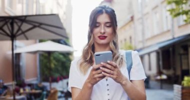Açık havada yürürken cep telefonu kullanan mutlu sarışın kadının portresini kapat. Şehir caddesinde kaydırırken ve telefon ekranına bakarken gülümseyen güzel kız. Gerçek hayat kavramı