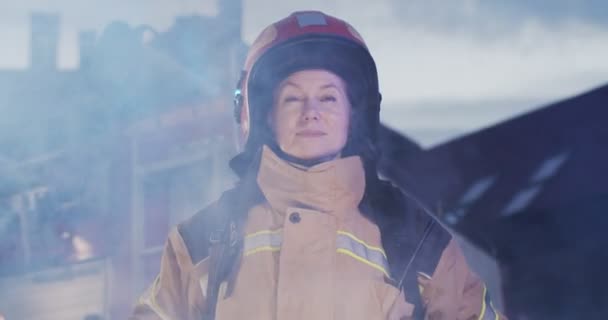 Portrait du beau pompier caucasien en casque et équipement de goéland debout à côté de la voiture la nuit en fumée du feu et regardant dans la caméra. Concept de sauver des vies, profession héroïque, sécurité incendie — Video