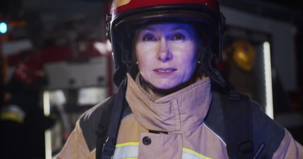 Portrait d'une jolie pompier caucasienne en casque et équipement de goéland debout à côté de la voiture et regardant dans la caméra. Le concept de sauver des vies, profession héroïque, sécurité incendie — Video