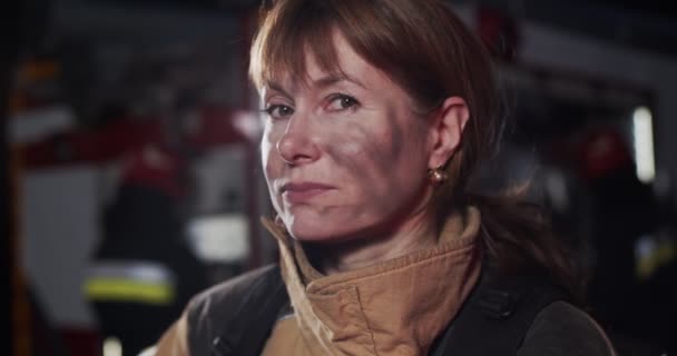 夜間にカメラをまっすぐに見る成熟した白人のブルネットの女性消防士の顔の肖像画を閉じます。命を救うという概念、英雄的な職業、火災安全 — ストック動画
