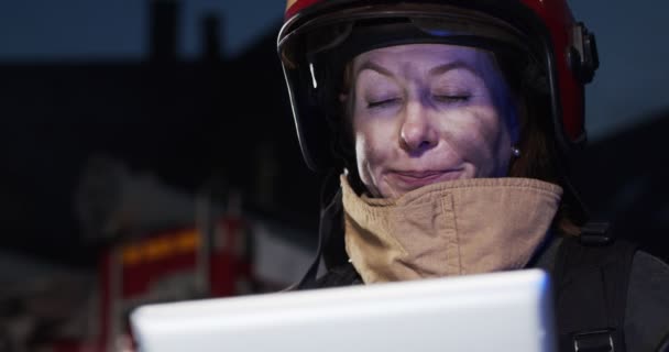 Gros plan portrait de femme blanche mûre jolie pompier regardant le dispositif de la tablette dans les mains debout à côté de la voiture de feu la nuit. Le concept de sauver des vies, profession héroïque, sécurité incendie — Video