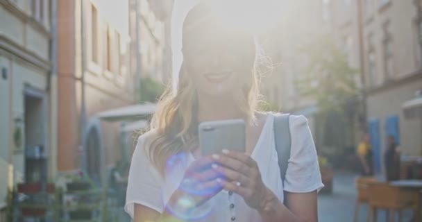 Gros plan portrait d'une femme bouclée souriante portant une robe tendance marchant dans la rue du centre-ville et utilisant son téléphone, naviguant sur Internet, lisant des nouvelles en ligne. Cocept de style de vie moderne — Video