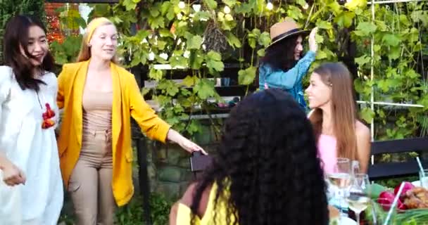 Multi-ethnic young man and women gathering together outdoors. African American and Caucasian beautiful girls sitting at table in garden. Joyful Asian girl hugging friends. Summer party concept — Stock Video