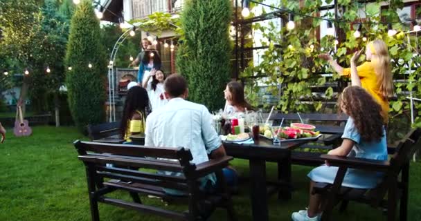 Multi-ethnic young people gathering together in garden. African American and Caucasian beautiful girls and guy sitting at table outdoor. Joyful Asian girl smiling. Summer party. Friends concept — Stock Video